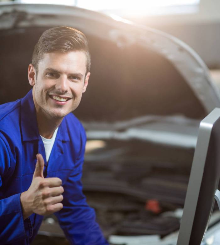 Portrait of mechanic showing thumbs up in repair garage